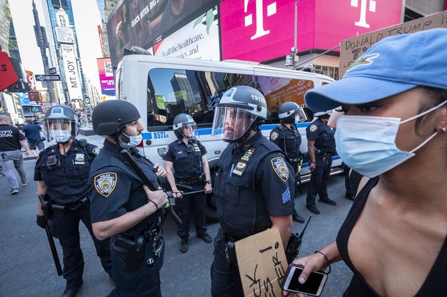 A protester wearing a mask walks past New York Police Department police officers while marching in Times Square in 2020.